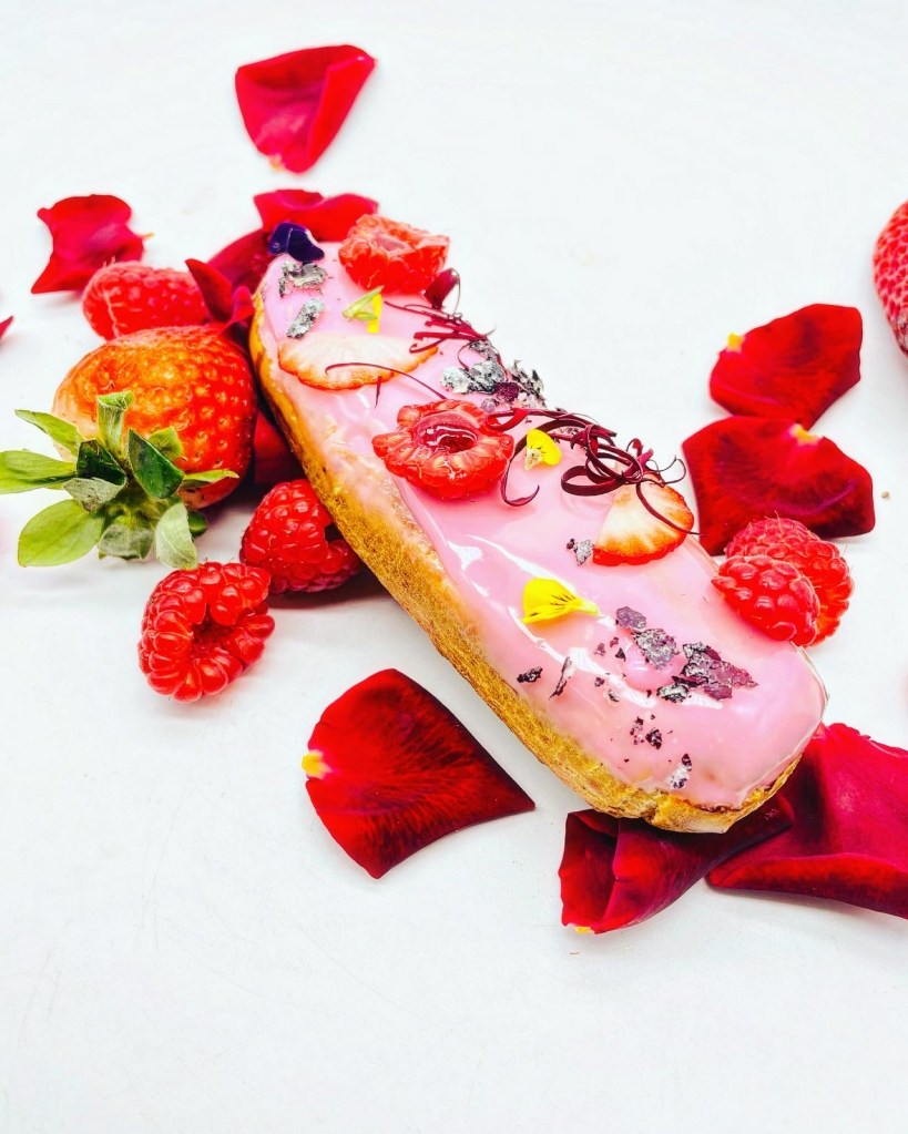 Petit coux cubierto de glaseado rosa, frambuesas, fresas y pétalos de rosa, relleno de una deliciosa crema. imagen con derechos de autor