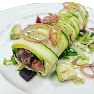 Canelón de aguacate relleno de tartar de atún fresco, acompañado de finas rodajas de cebolla encurtida, dados de remolacha y brotes de rúcula crujiente. Una presentación delicada y llena de sabor, ideal para quienes buscan opciones ligeras y gourmet en sus eventos privados. Perfecto para una experiencia de alta cocina.