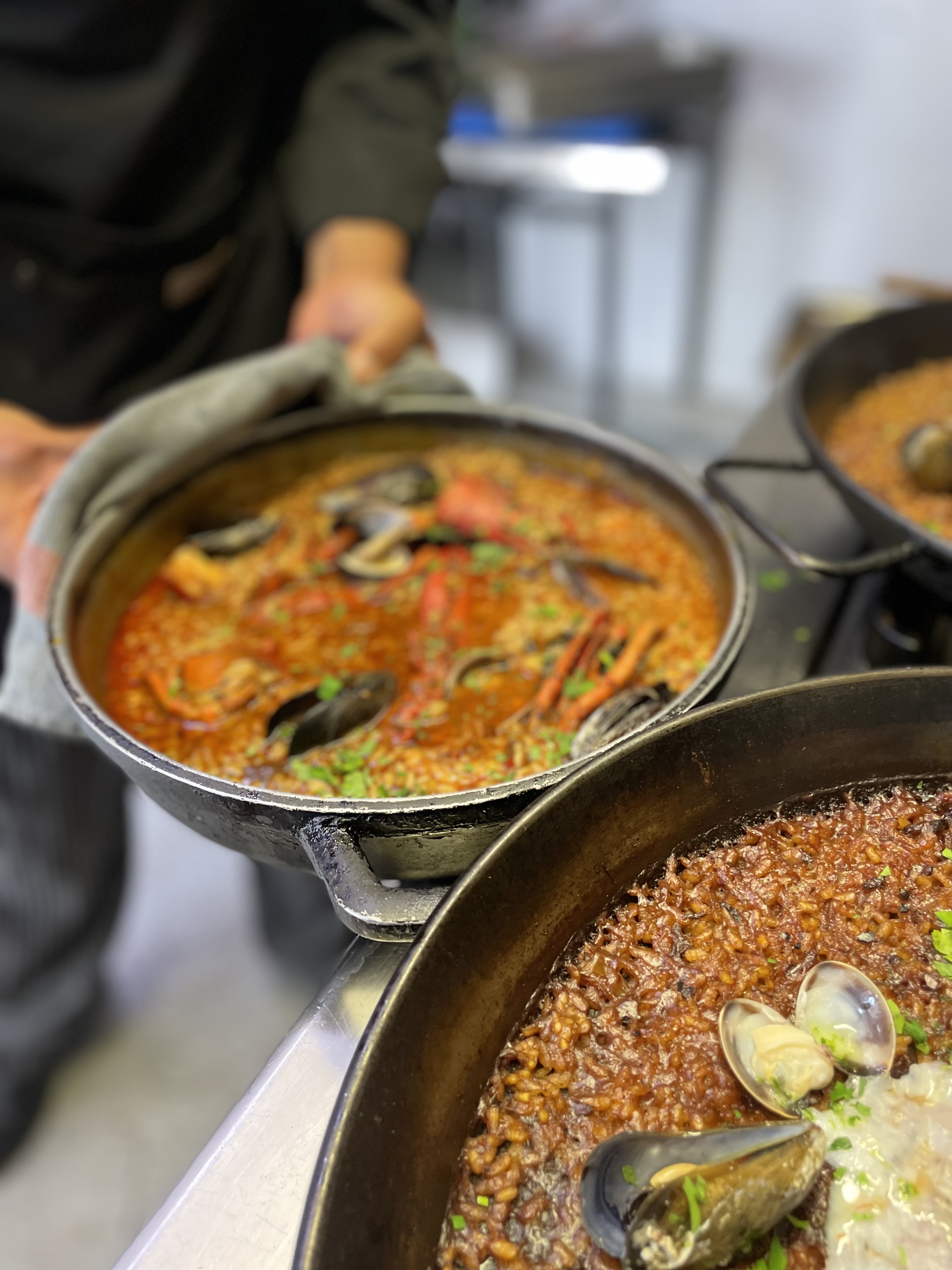 La imagen muestra diferentes paellas, con diferentes tipos de arroces del mundo, todos con tonos doramos y sobre el, navajas, gambas, perejil, cangrejo, todas recién hechas.