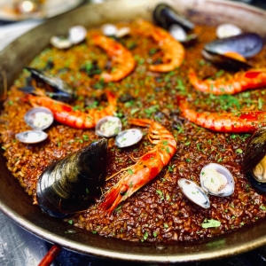 La imagen muestra una paella de marisco recién preparada, con un arroz de tono dorado y ligeramente tostado, decorado con gambas enteras, mejillones de concha negra y almejas distribuidas de forma equilibrada. La textura del arroz, junto con el color intenso del sofrito y el toque de perejil fresco, transmite una receta auténtica de la cocina mediterránea. Es una fotografía ideal para contenidos sobre gastronomía española, restaurantes, recetas tradicionales, turismo culinario y cocina valenciana.